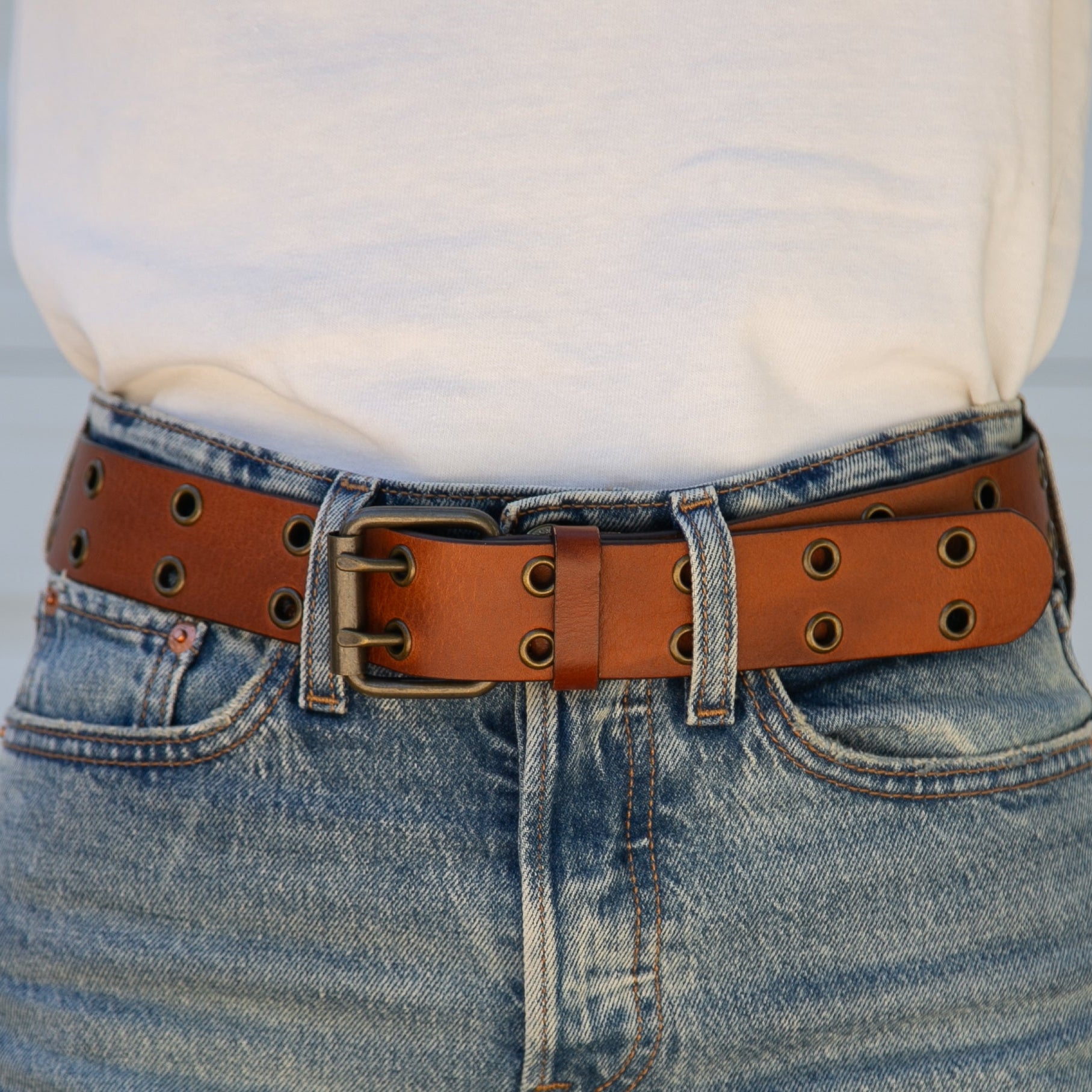 Person wearing blue jeans with a brown leather belt against a light background