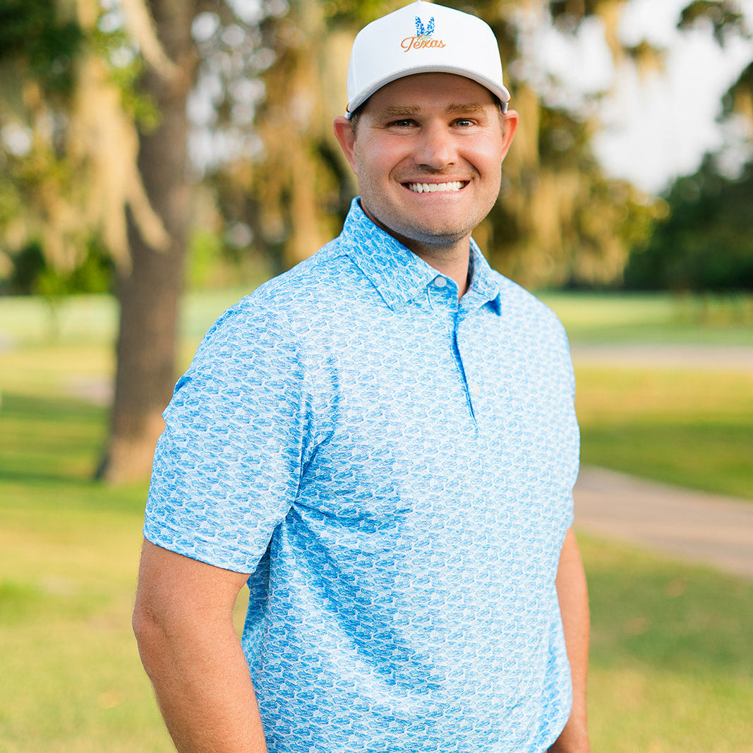 Man wearing a blue shirt and white cap standing on a grassy area with trees in the background