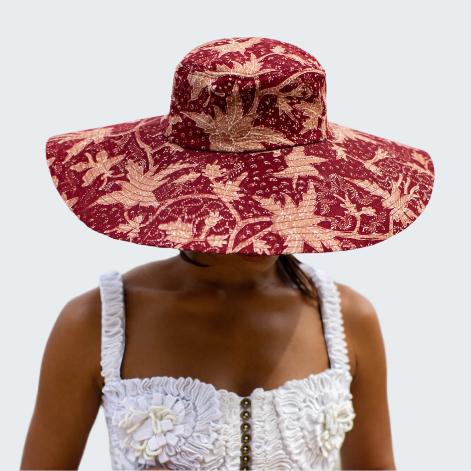 Person wearing a red floral sun hat with a blurred beach background