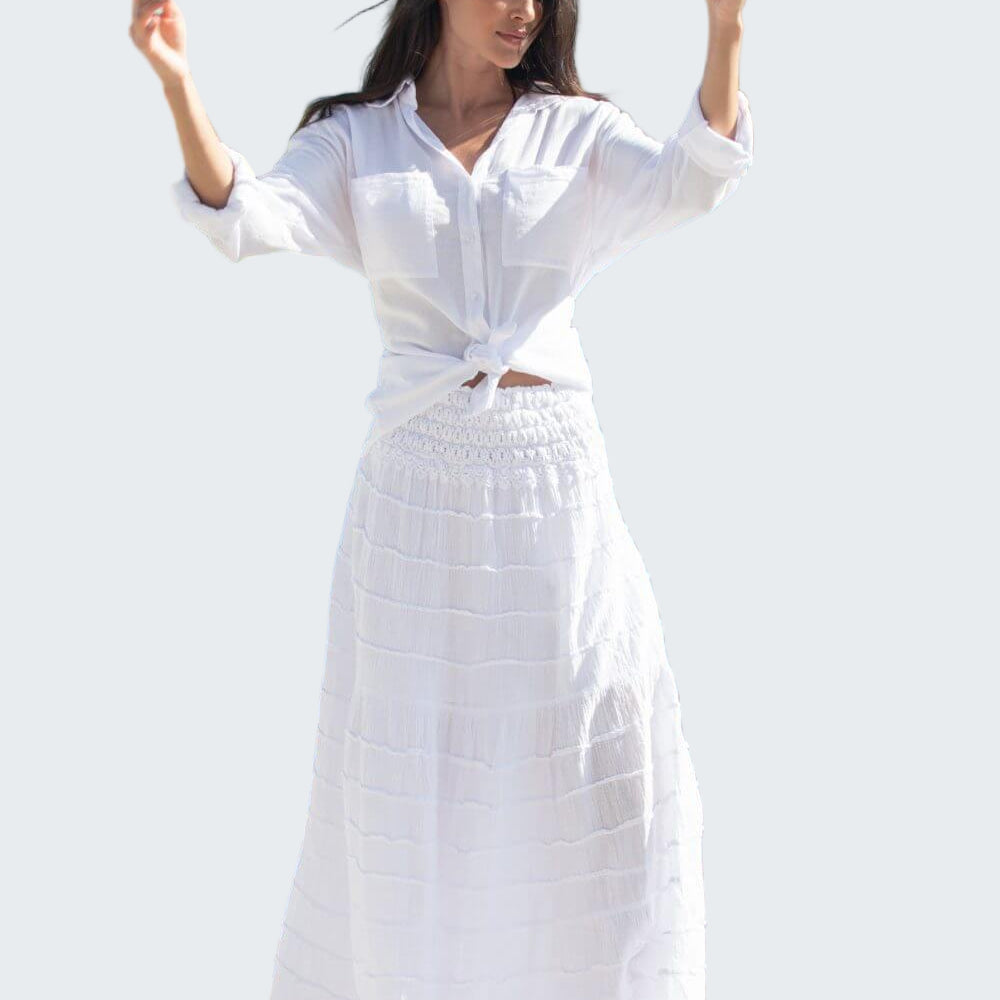 Woman in a white dress standing by a waterfront with buildings in the background