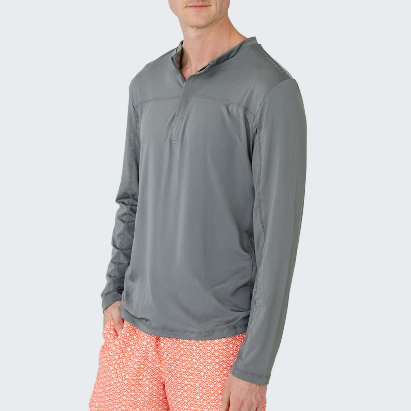 Man wearing a gray long-sleeve shirt and pink shorts with a white pattern on a light gray background