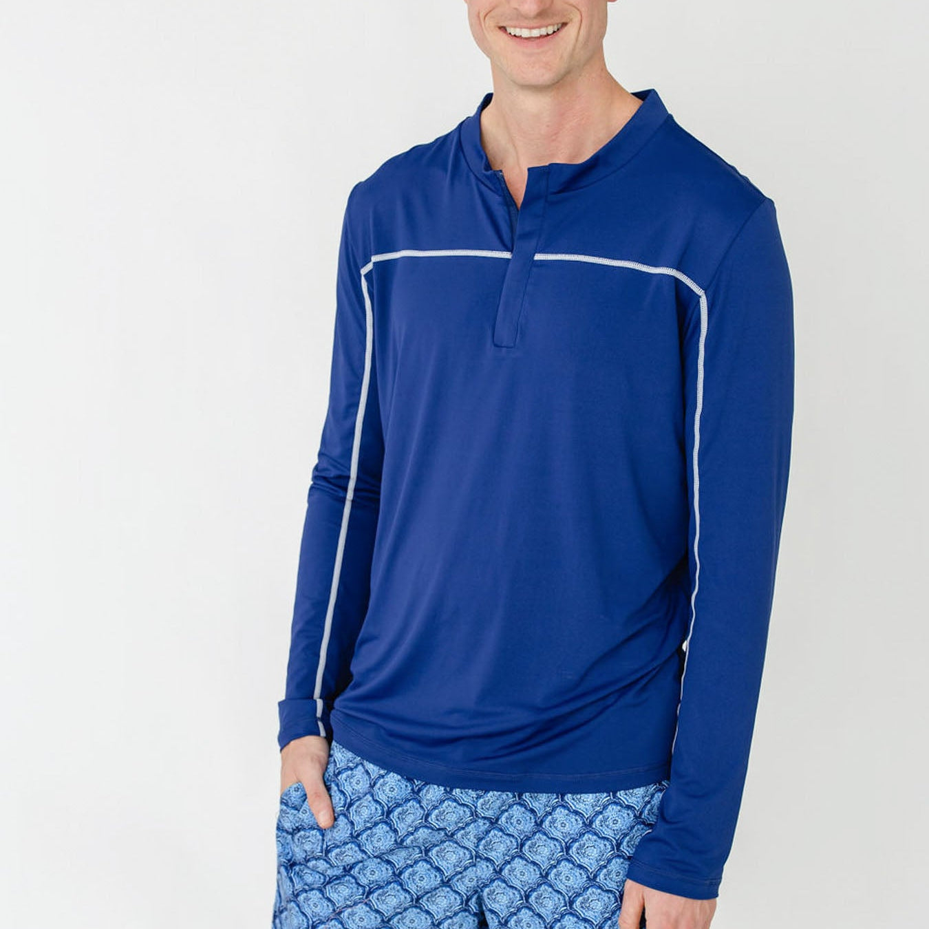 Man wearing a blue long-sleeve shirt and patterned shorts on a white background