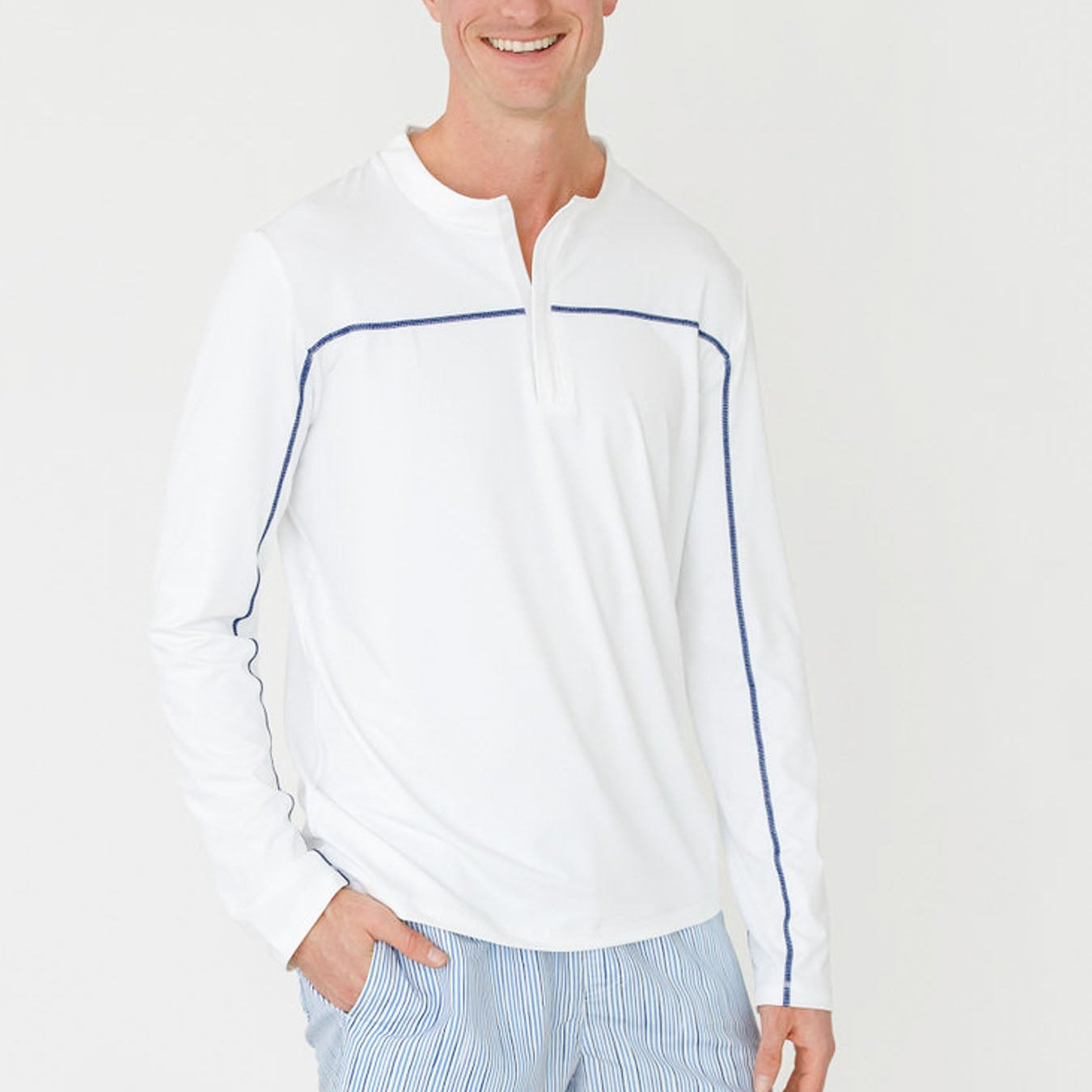 Man wearing a white long-sleeve shirt with blue accents and light blue shorts on a white background