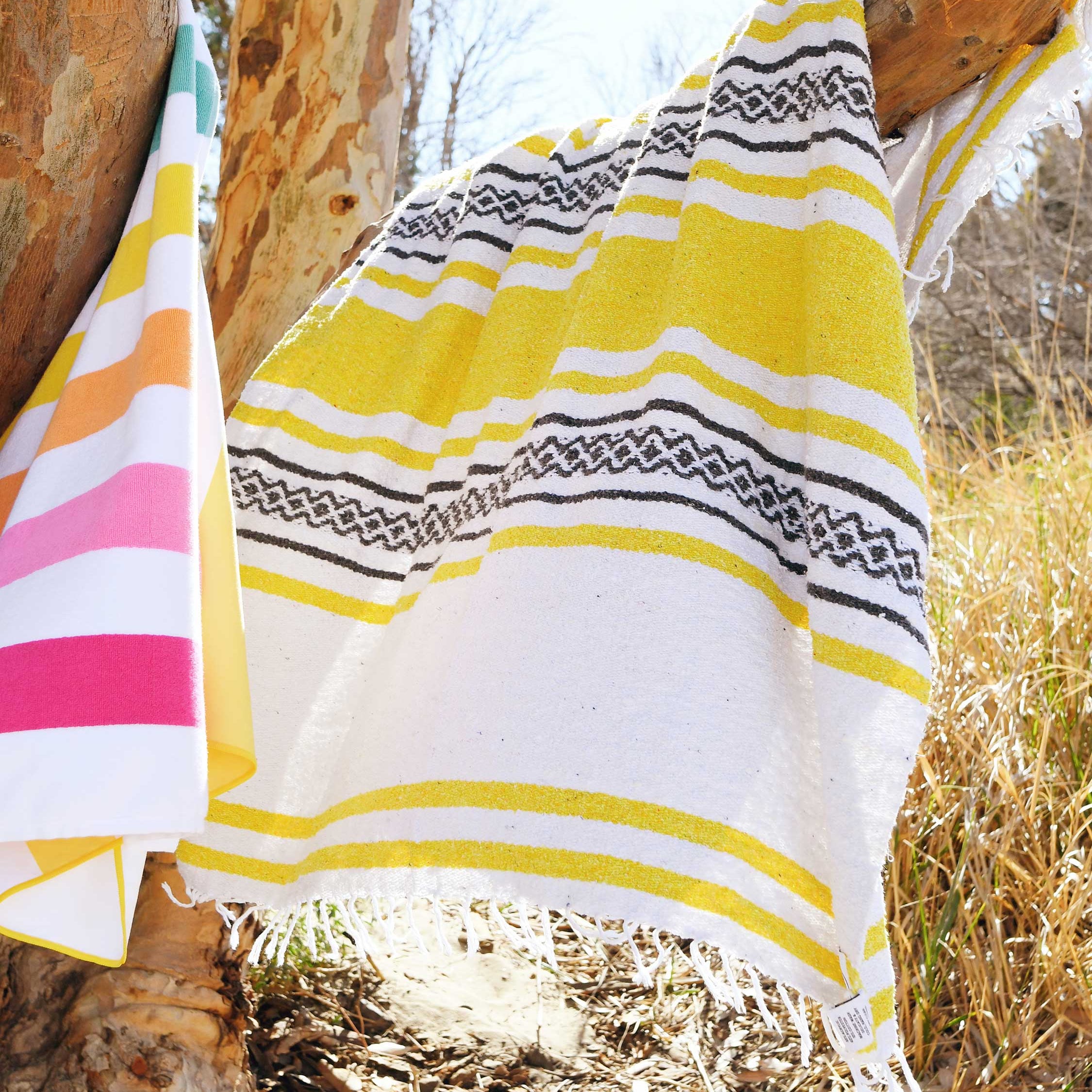 Yellow and white striped towel with geometric pattern draped over a wooden post outdoors.