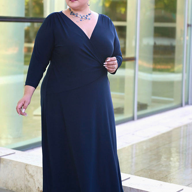 Woman wearing a navy blue dress standing outdoors with a glass building in the background