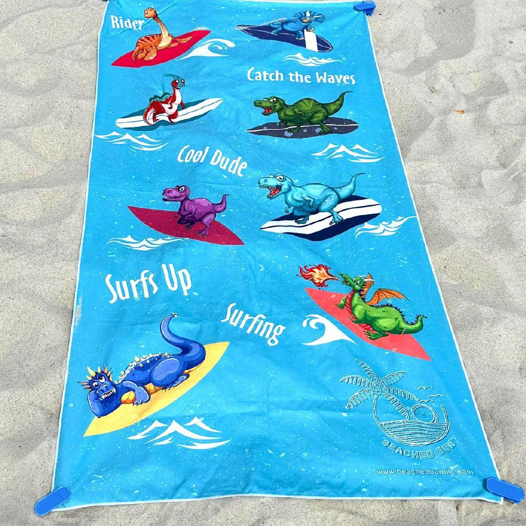 Blue beach towel with dinosaur graphics on a sandy background