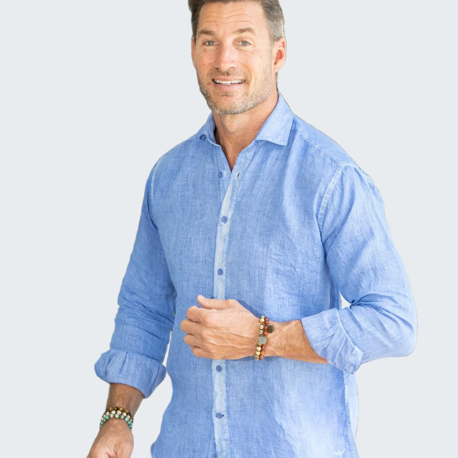 Man wearing a light blue shirt and white pants standing outdoors with plants in the background