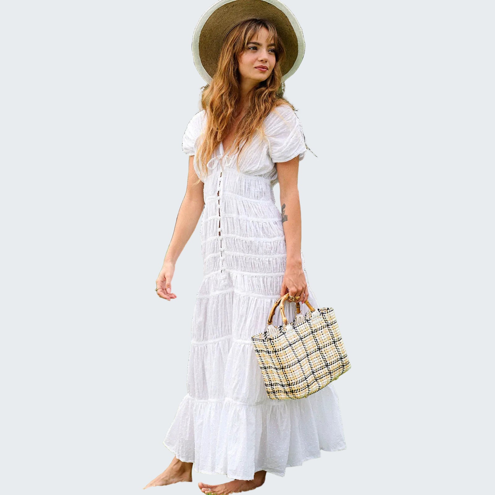 Woman in a white dress and straw hat holding a patterned handbag in a garden setting