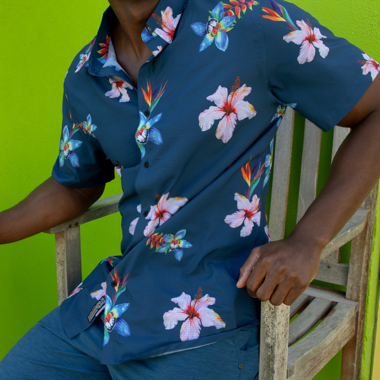 Person wearing a navy blue floral shirt and shorts against a green background
