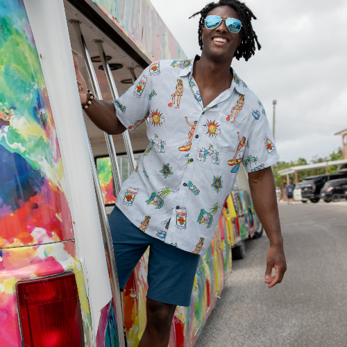 Man in a colorful shirt and sunglasses standing next to a vibrant, artfully painted vehicle.