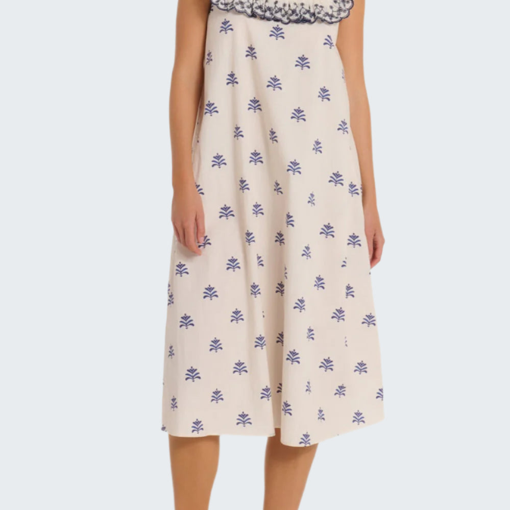 Woman wearing a white dress with blue floral patterns on a plain background