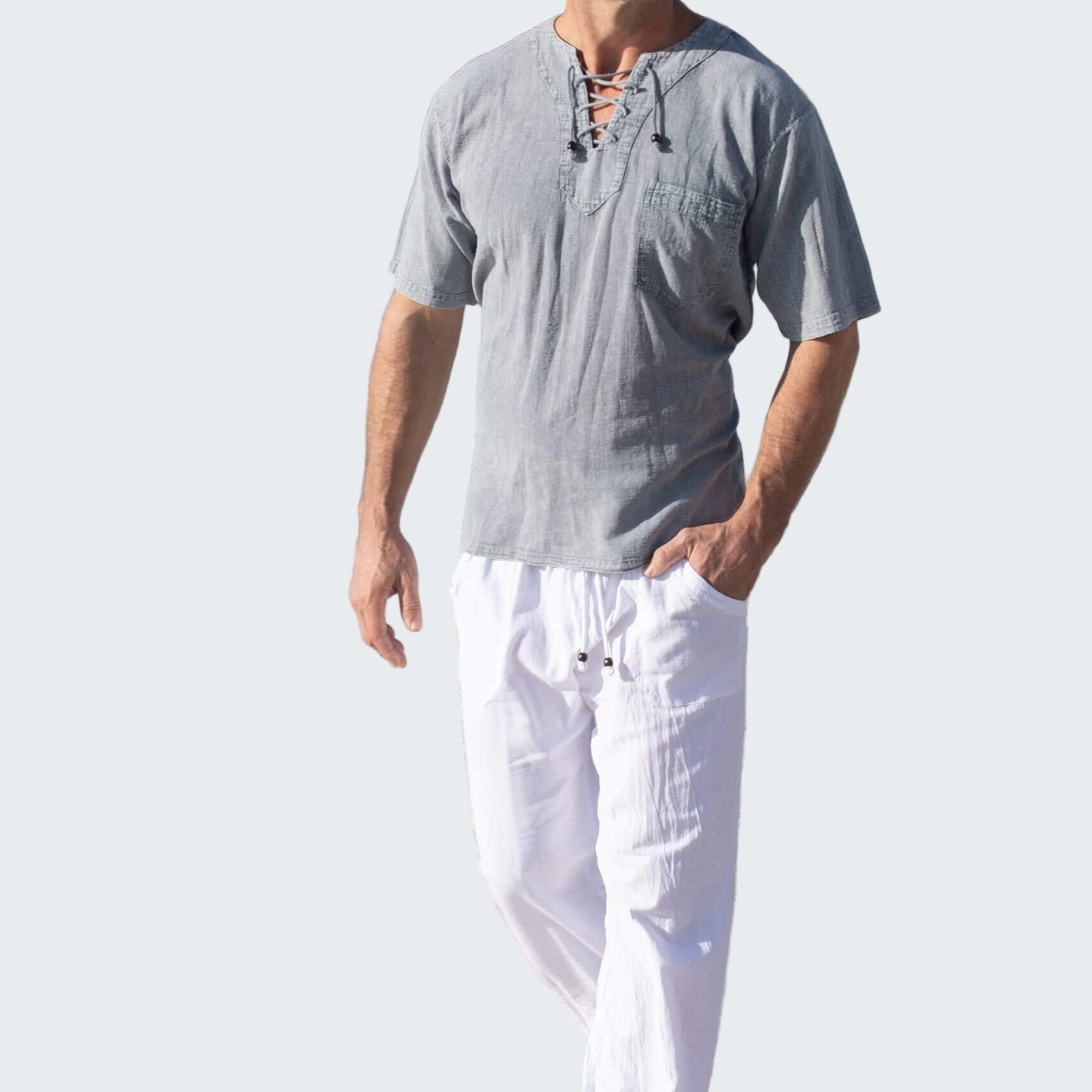 Man walking on a beach wearing a gray shirt and white pants.