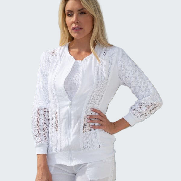 Woman wearing a white lace top and pants by a body of water with trees in the background