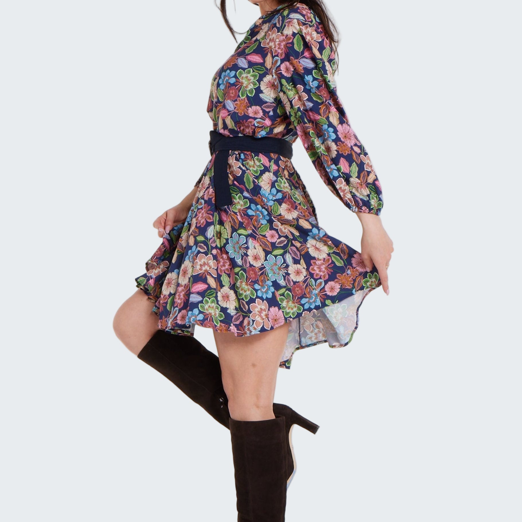Woman wearing a floral dress with long sleeves and knee-high black boots on a white background
