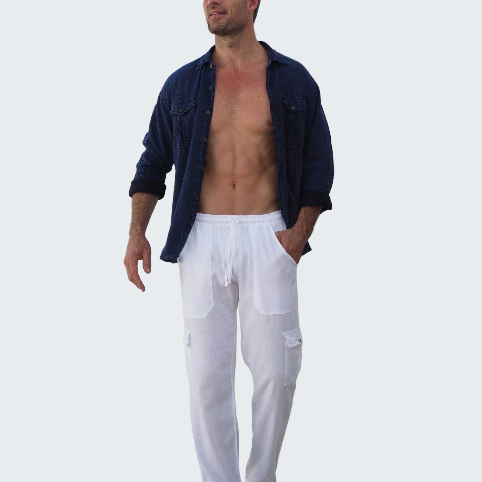 Man wearing a blue shirt over white pants standing on a wooden deck with a white wall and wooden door in the background.