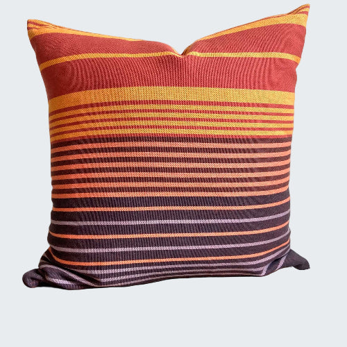 Striped pillow with red, orange, and purple colors on a wooden stool against a white wall.
