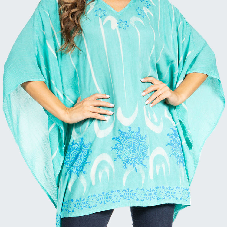 Turquoise poncho with white patterns worn by a person on a white background
