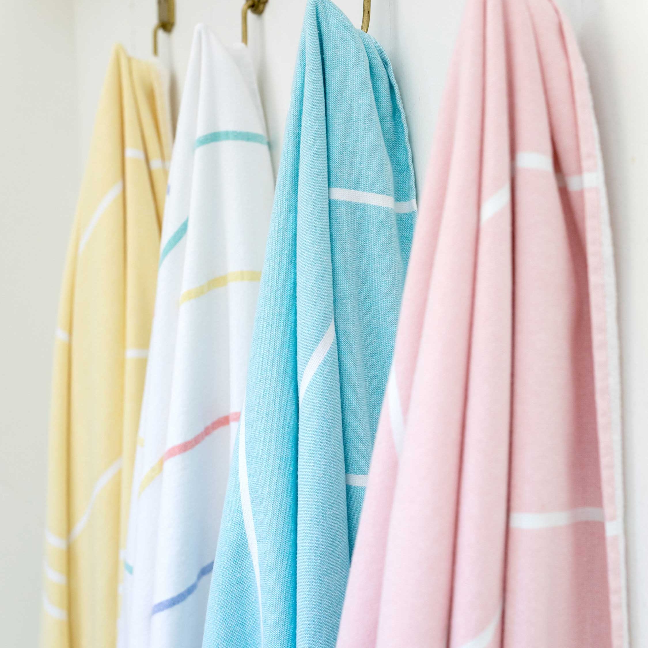 Four pastel-colored towels hanging on a rack against a white wall.