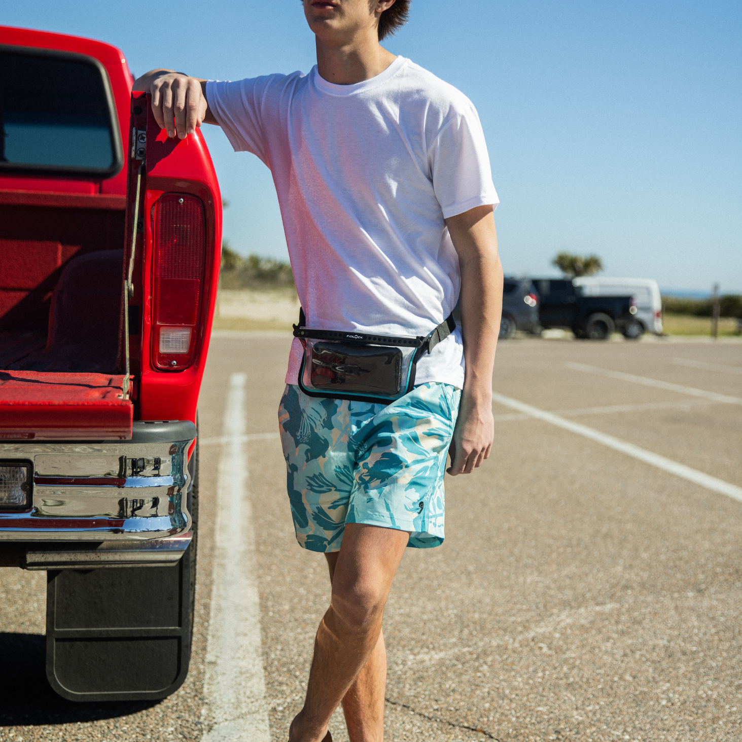 Man standing next to a red truck wearing a white t-shirt, green shorts, and sunglasses.