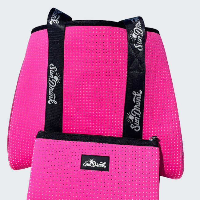 Pink textured bag with black straps and 'Sun Dune' logo on a sandy beach.