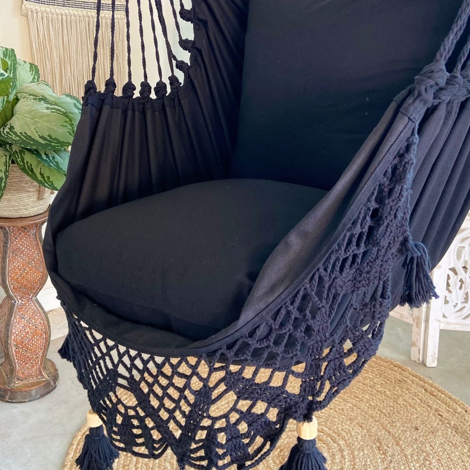 Black hammock chair with tassels on a textured floor