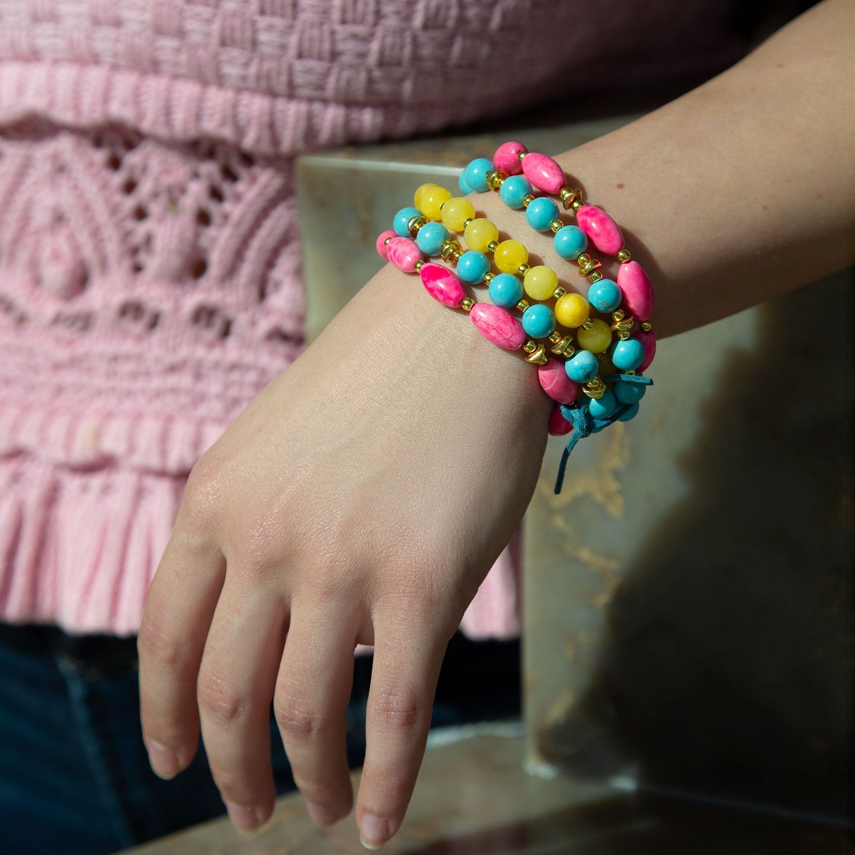 Colorful beaded bracelet on a wrist with a pink textured sweater in the background
