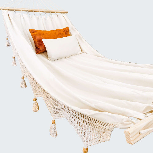 White hammock with orange and white pillows against a decorative wall.
