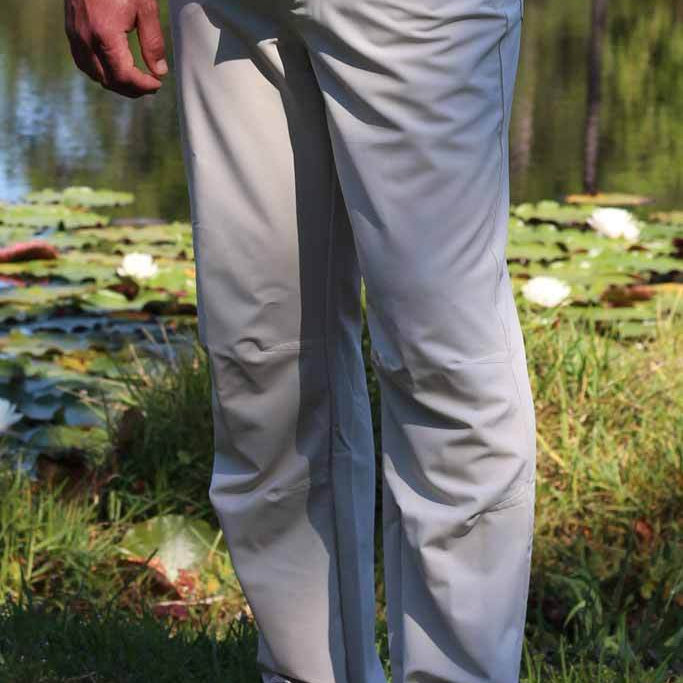Person wearing light gray pants and a turquoise shirt standing in a natural setting with water and plants.