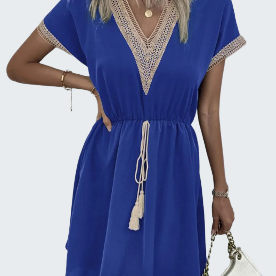 A model wearing a blue v-neck short sleeve dress with tassel detailing, paired with a white accessory.
