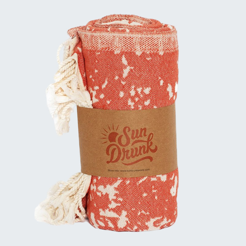 Roll-up beach towel with white floral pattern on a red background, branded 'Sun Drunk', on a white background.