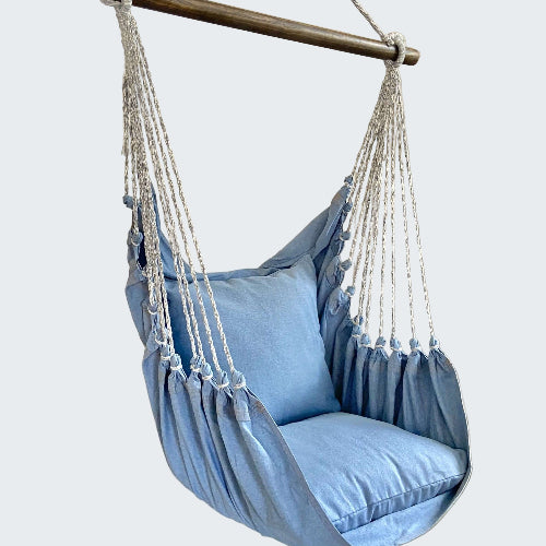 Blue hammock chair with white ropes in a room with a plant and candle.