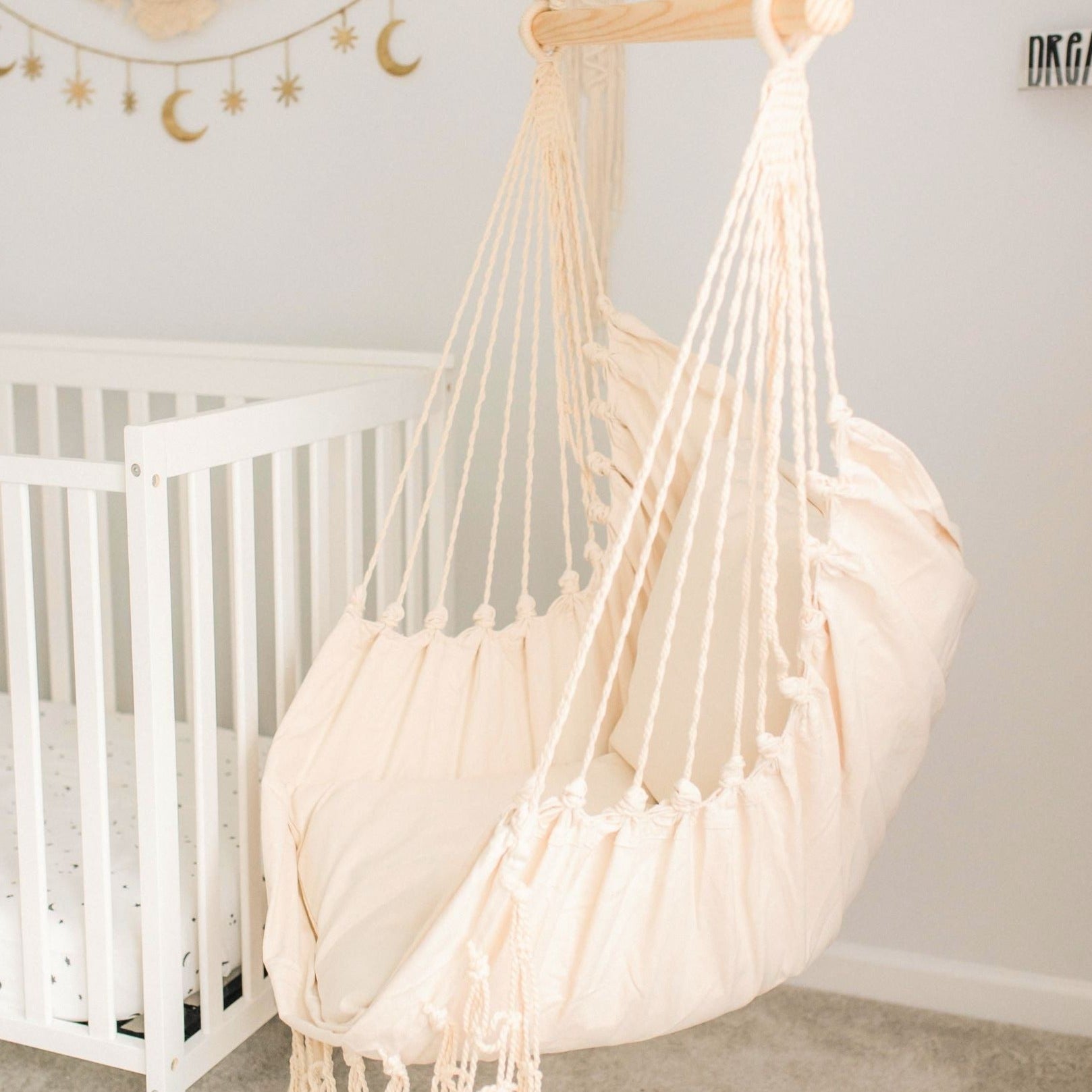 White hammock chair in a nursery with a crib and decorative items on the wall.