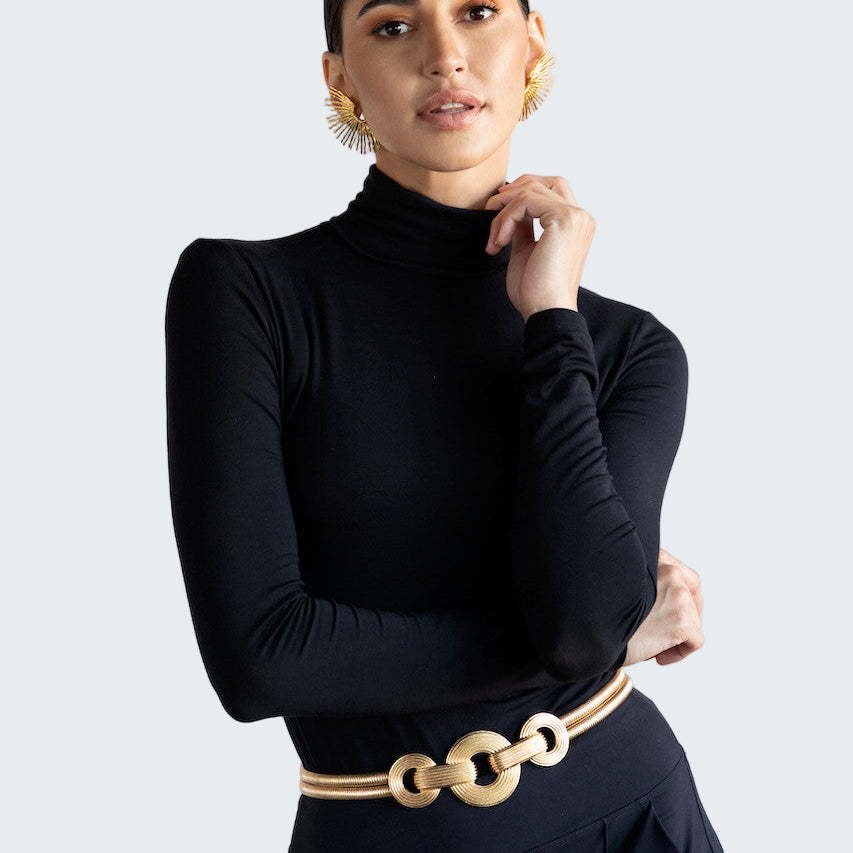 Woman wearing a black turtleneck and gold belt against a white background