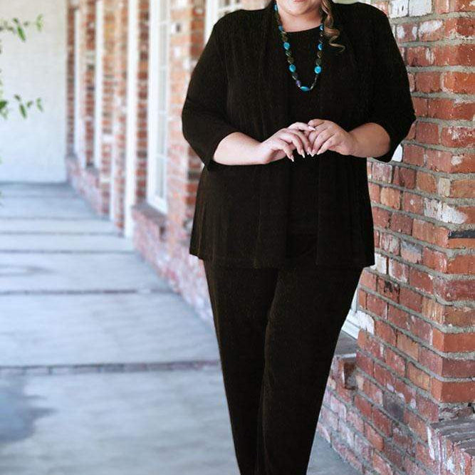 Woman in a black outfit standing against a brick wall.
