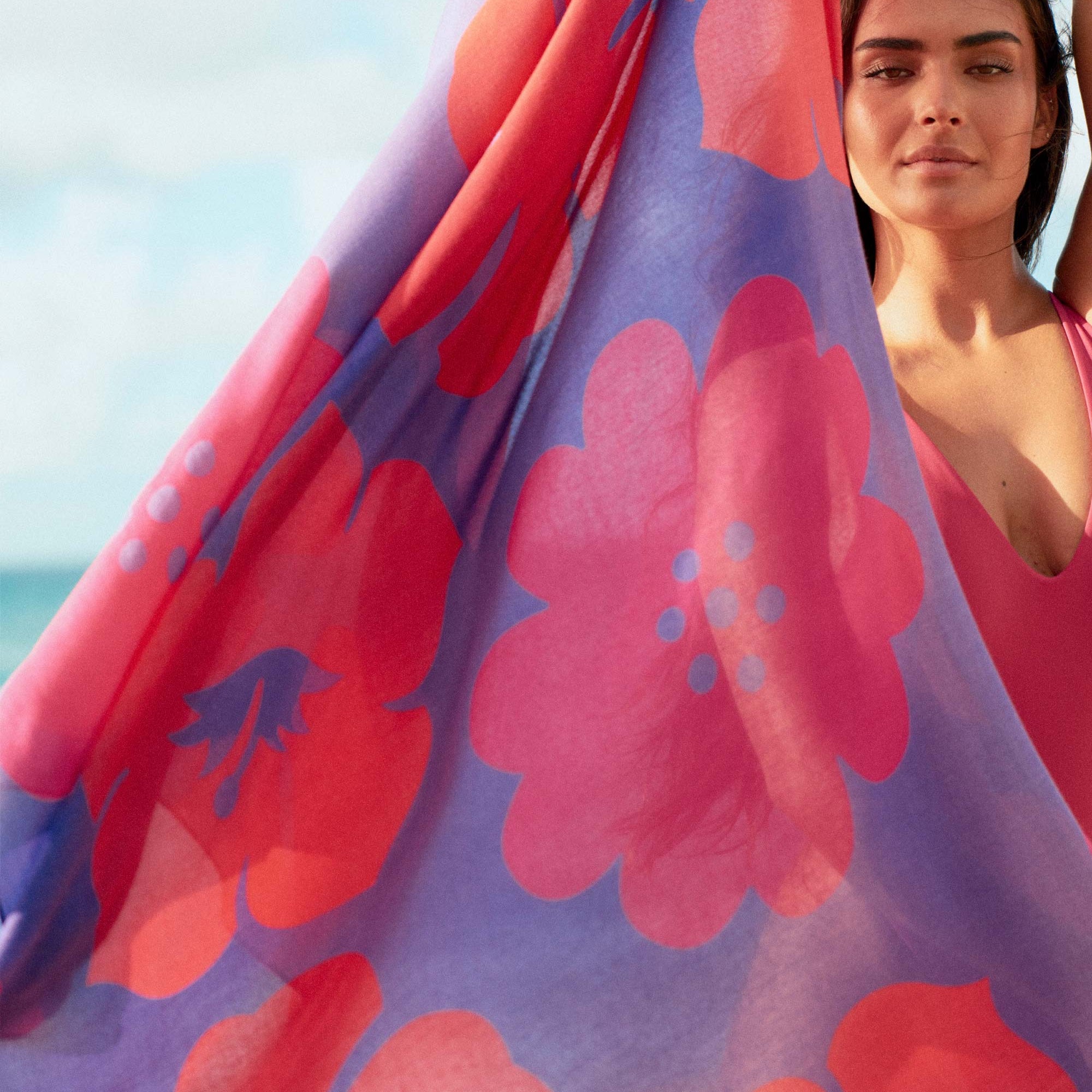 Woman holding a colorful floral towel with a beach in the background