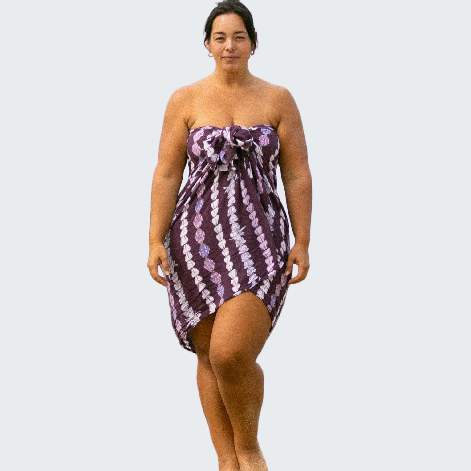 Woman in a purple patterned dress standing on a rock by the ocean.