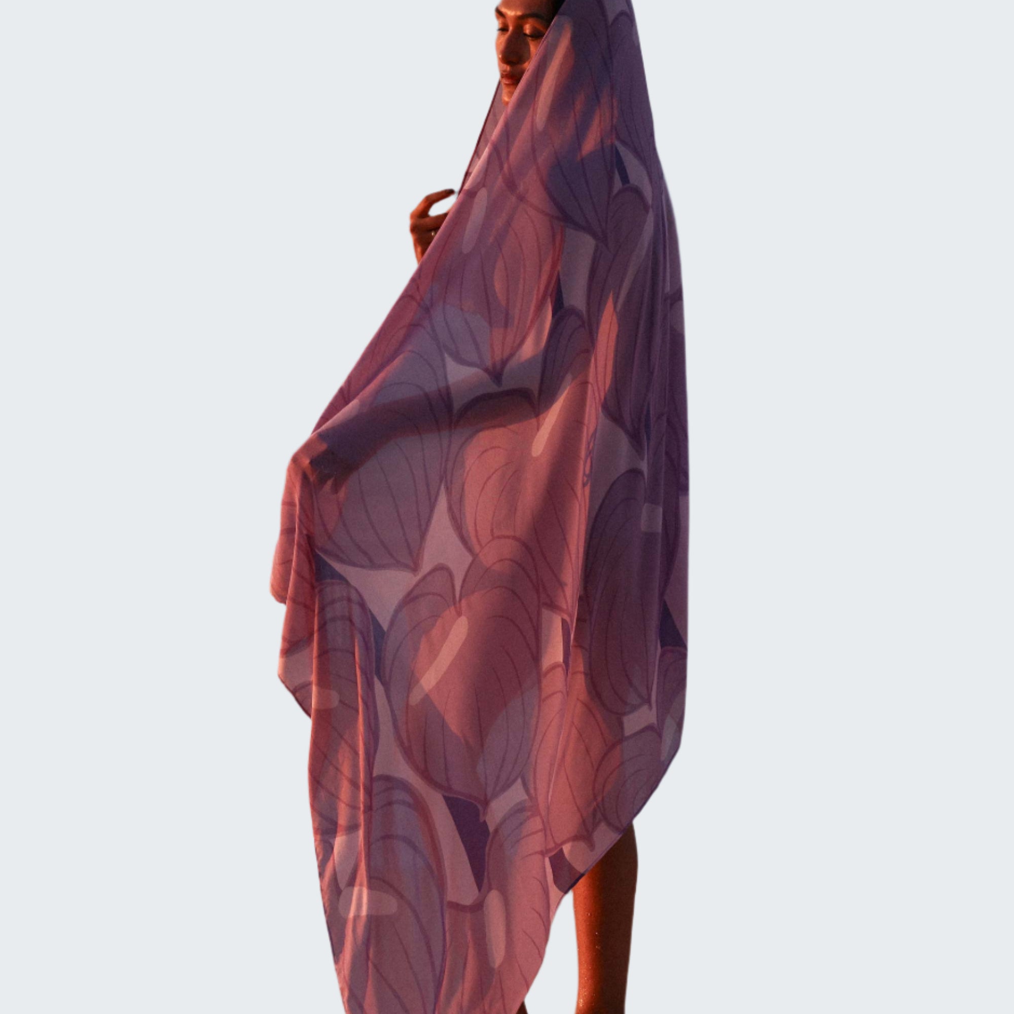 Person wrapped in a purple patterned towel on a beach with ocean waves in the background