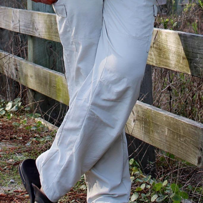 Person wearing light gray pants and sandals standing near a wooden fence.