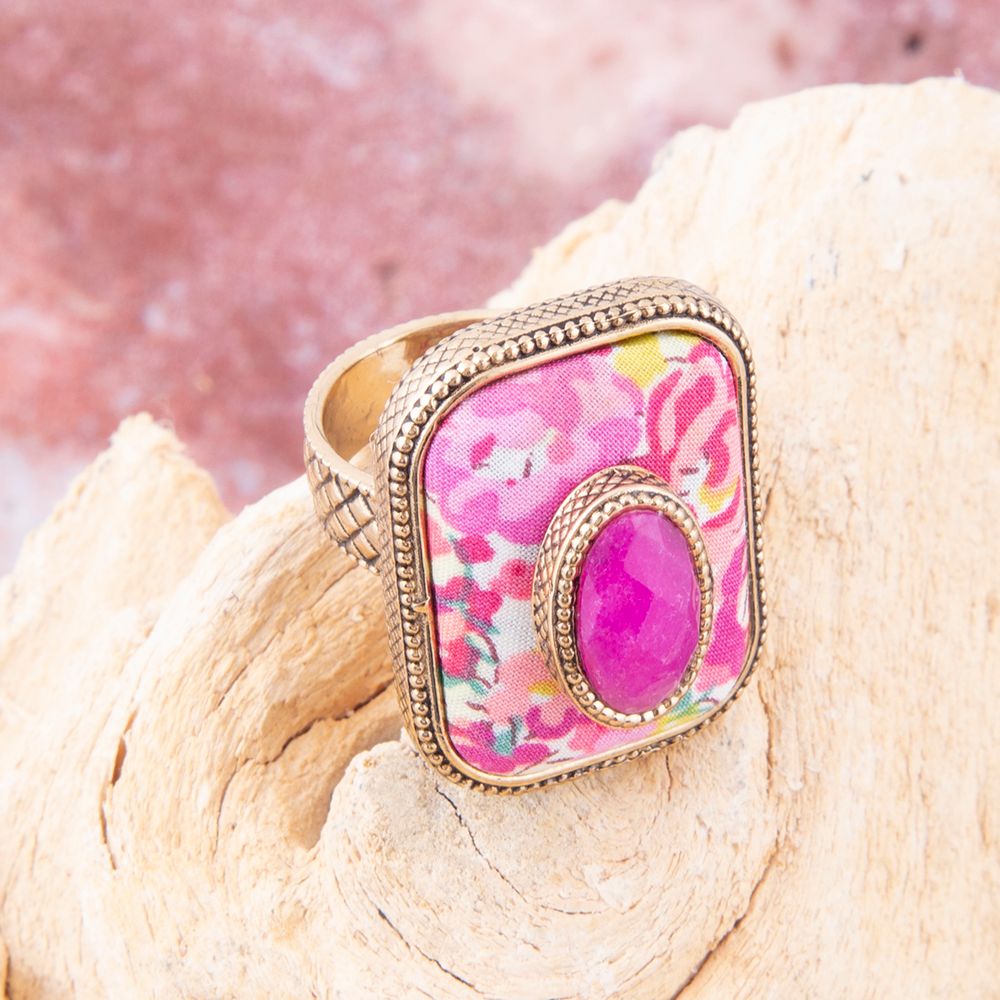 Ring with pink floral design and gold frame on a wooden surface