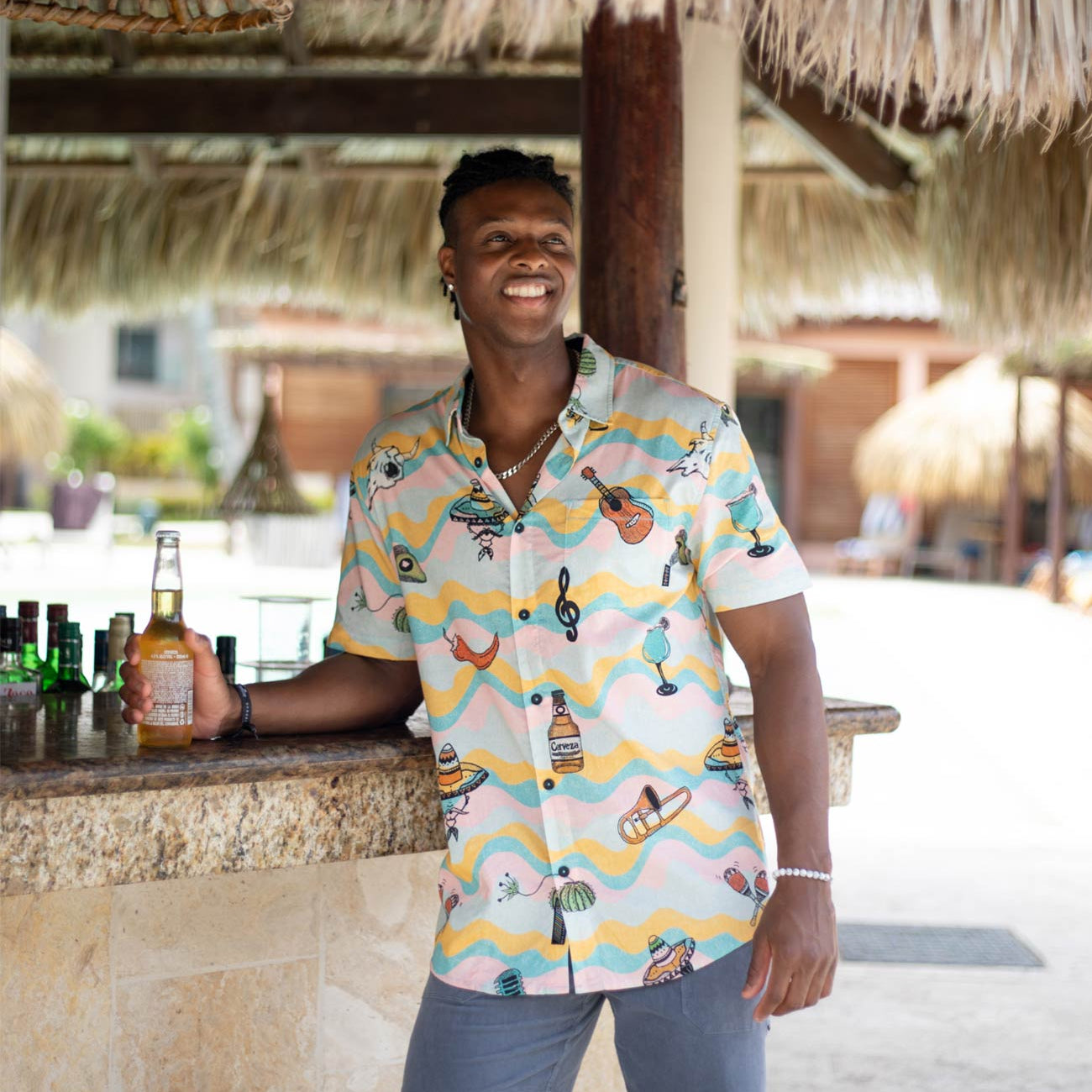 Man in a colorful shirt standing at a bar with a thatched roof