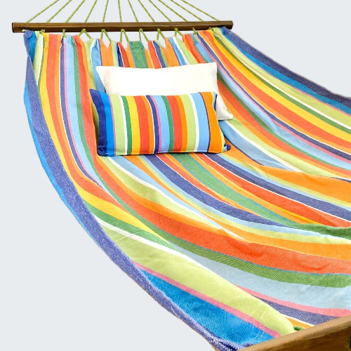 Colorful striped hammock with pillows on a wooden stand against a white curtain background.