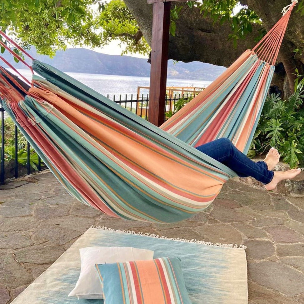 Person relaxing in a colorful striped hammock with a scenic background