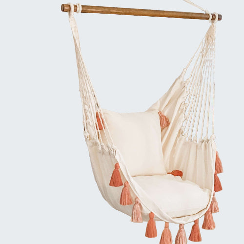 White hammock chair with pink tassels hanging in a room with a decorative screen and plant.