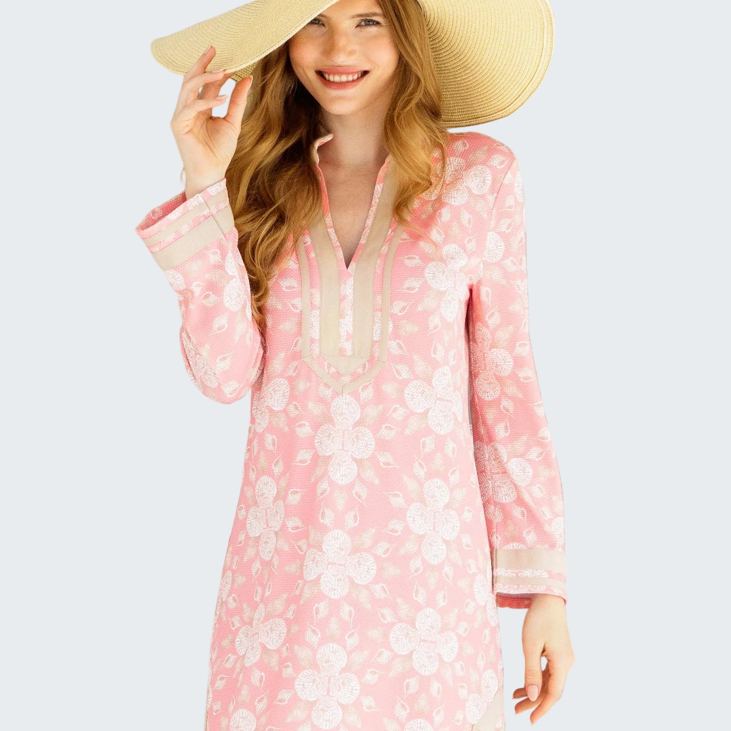 Woman wearing a pink floral dress and beige hat in front of a glass door.