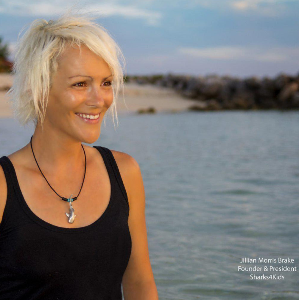 Woman with blonde hair and a black tank top standing by a body of water, with 'Sharks4Kids' branding.