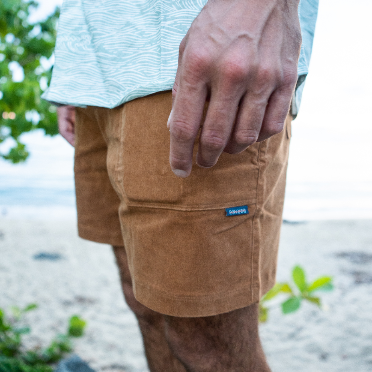 Person wearing brown shorts with a visible brand logo on a beach.