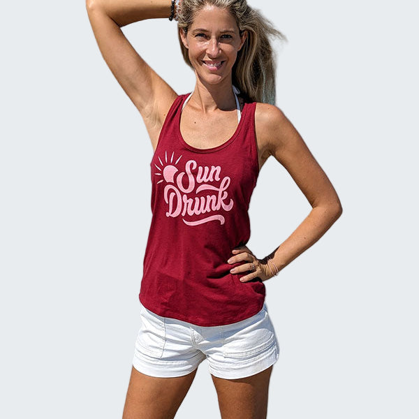 Woman wearing a red tank top with 'Sun Drunk' text on a beach
