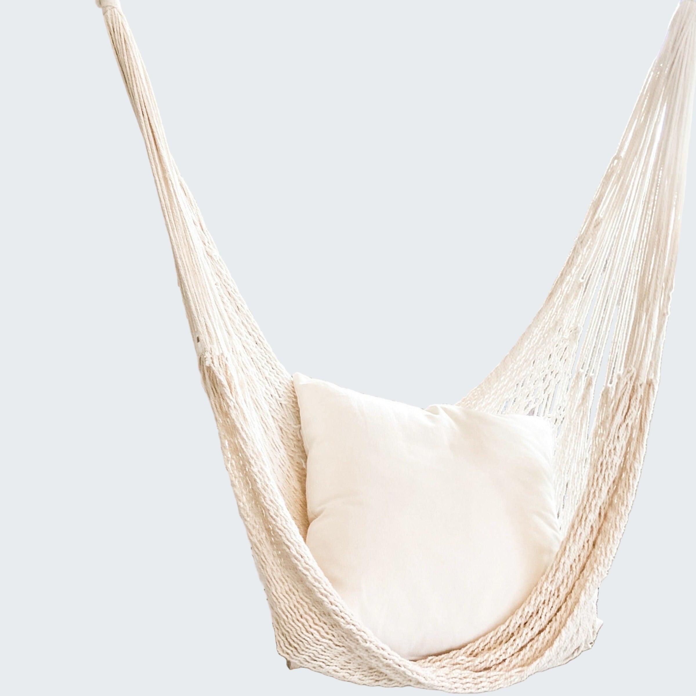 Beige hammock chair with a white pillow in a room with decorative screen and plant.