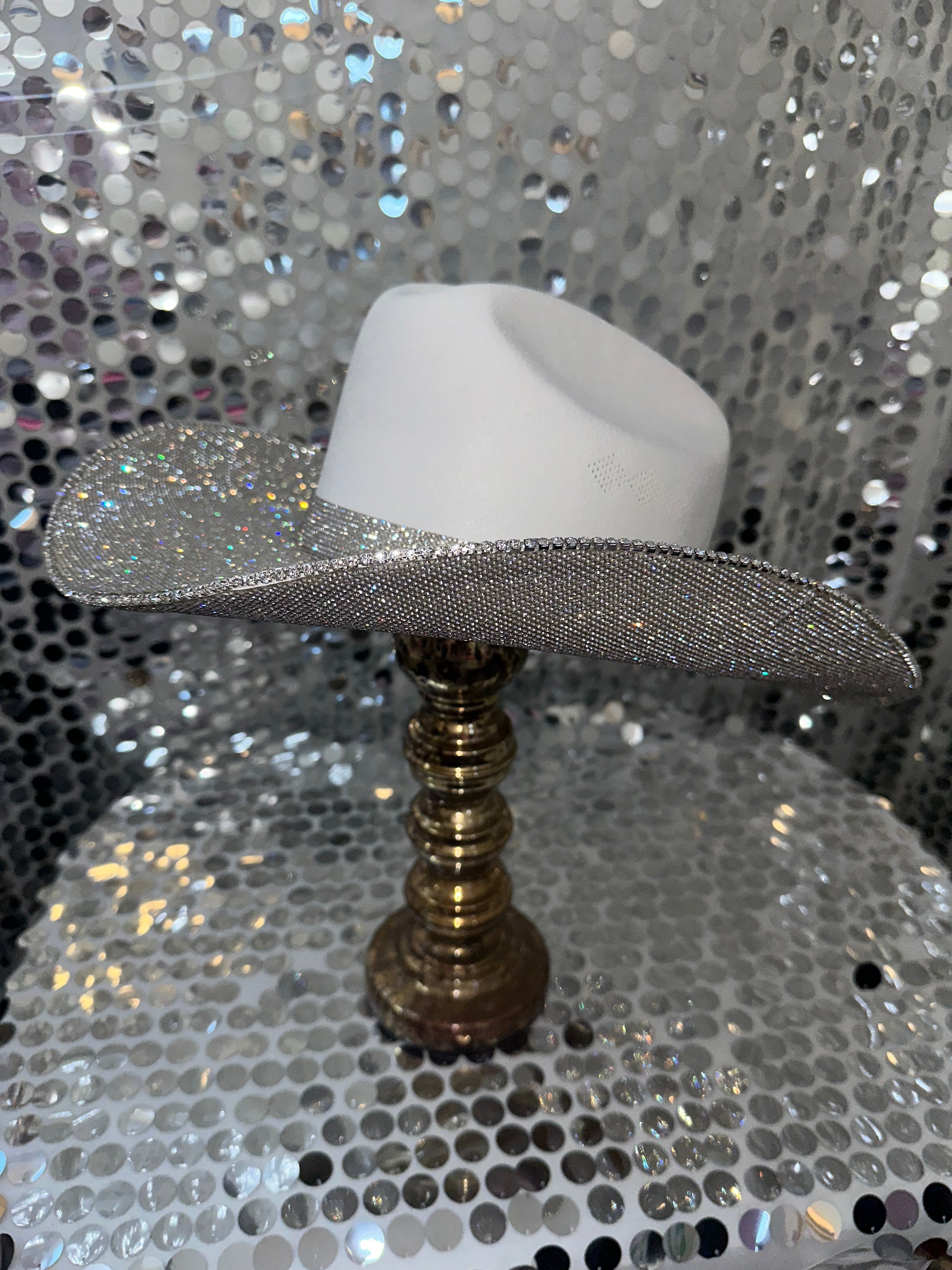 White cowboy hat with a silver glitter band on a gold stand against a silver sequin background