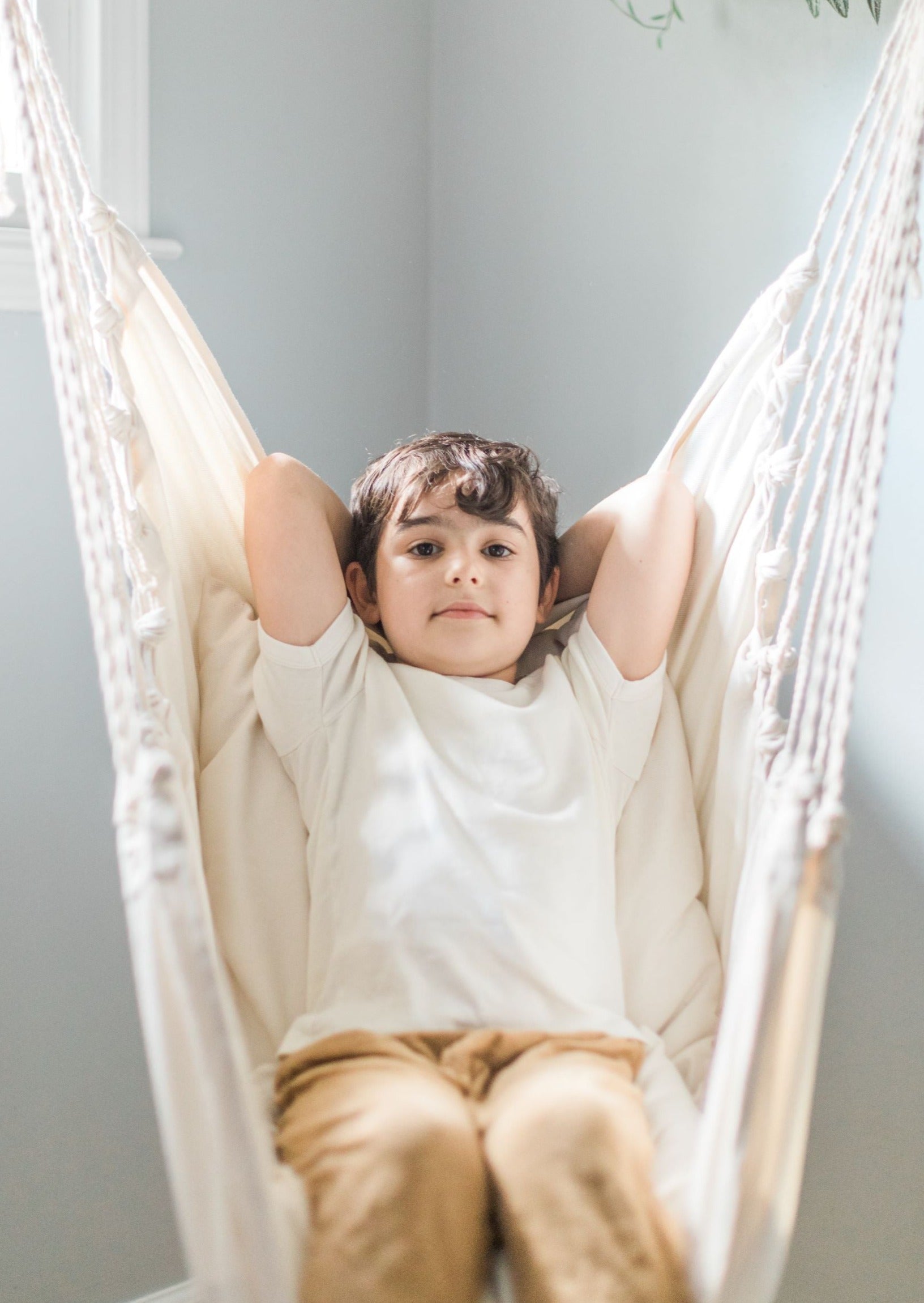 Child sitting in a white hammock against a light gray wall